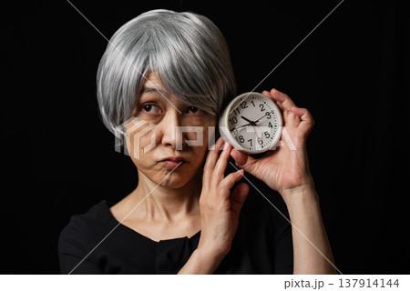 目覚まし時計を持ち口をとがらせる白髪のシニア女性 137914144