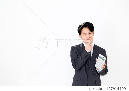電卓を持って悩むスーツを着たミドル男性ビジネスマン 電卓を持って悩むスーツを着たミドル男性ビジネスマン 137914300