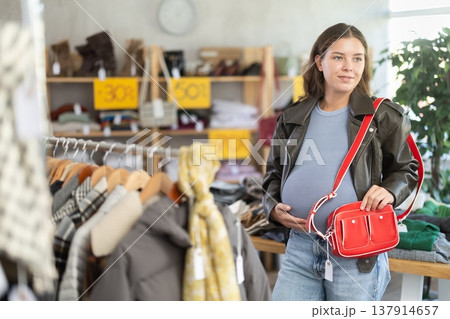 Pregnant woman choosing handbag in clothing store Pregnant woman choosing handbag in clothing store 137914657