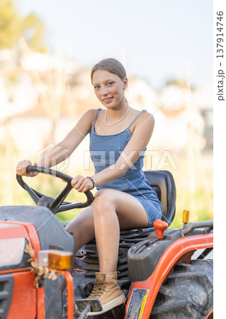 Young woman sits on minitractor and drives rural vehicle, performs loading work on farm 137914746