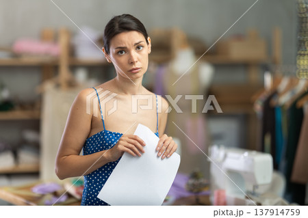 Upset woman seamstress with documents in workshop Upset woman seamstress with documents in workshop 137914759