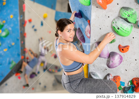 Smiling sporty young girl climbing on artificial bouldering wall 137914829