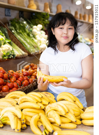 Young girl choosing fresh bananas in fruit and vegetable section of supermarket Young girl choosing fresh bananas in fruit and vegetable section of supermarket 137915011