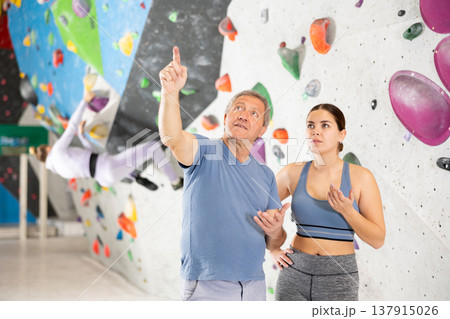 Interested young girl and elderly man talking near bouldering wall Interested young girl and elderly man talking near bouldering wall 137915026