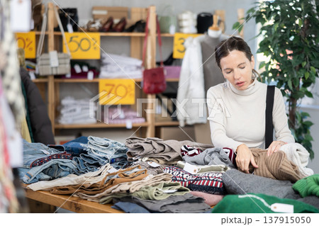 Attentive middle-aged woman choosing sweater in clothing store 137915050