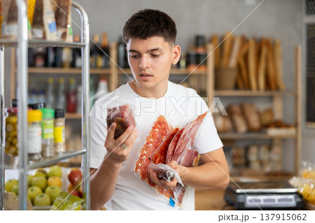 Guy carefully selects and buys dried meat and dried sausage in grocery store 137915062