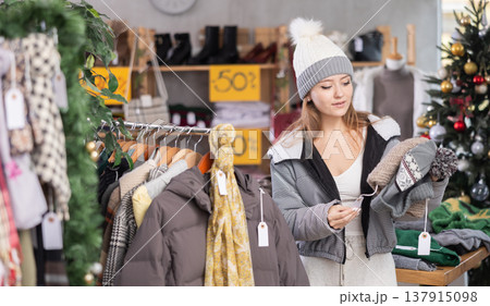 Girl client looks at products in store, looks closely at hat, picks up wardrobe item Girl client looks at products in store, looks closely at hat, picks up wardrobe item 137915098