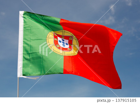 Beautiful large red and green Portuguese flag waving in wind against blue sky. 137915105