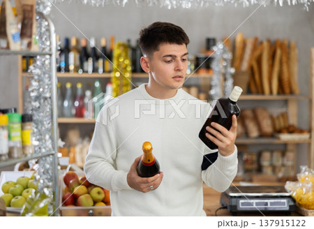 Young guy is choosing spark wine and whiskey in grocery store during New Year Young guy is choosing spark wine and whiskey in grocery store during New Year 137915122