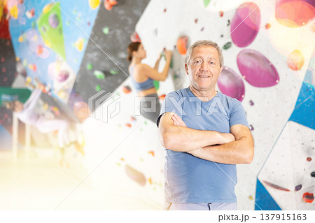 Portrait of positive elderly male coach against background of climbing wall 137915163