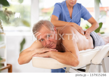 Relaxed old man having back massage therapy conducted by skilled masseuse 137915266