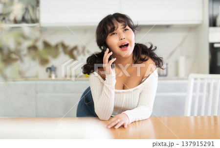 Cheerful girl chatting with friends on phone in home kitchen 137915291