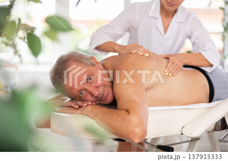 Relaxed old man having back massage therapy conducted by skilled masseuse 137915333