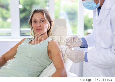 Middle-aged woman having arm injection lying on clinical chair Middle-aged woman having arm injection lying on clinical chair 137915493