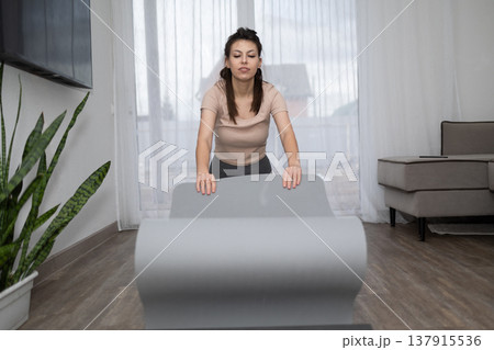 Woman Unrolling Yoga Mat in Her Living Room for an at Home Workout Woman Unrolling Yoga Mat in Her Living Room for an at Home Workout 137915536