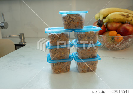 Stack of blue plastic containers filled with homemade pet food on kitchen counter. Preparing nutritious meals for dogs from fresh ingredients. Healthy animal feeding and pet care concept. photography Stack of blue plastic containers filled with homemade pet food on kitchen counter. Preparing nutritious meals for dogs from fresh ingredients. Healthy animal feeding and pet care concept. photography 137915541