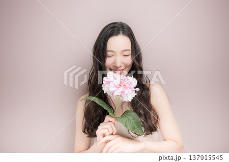 ダリアの花を持って多幸感にあふれるピンクの春色イメージの女性の美容ビューティーイメージ　ピンク背景 137915545