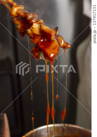 焼き鳥の串をタレ鍋から引き上げるシーン タレが滴る瞬間 ドラマチックな照明 居酒屋・屋台イメージ 137917131