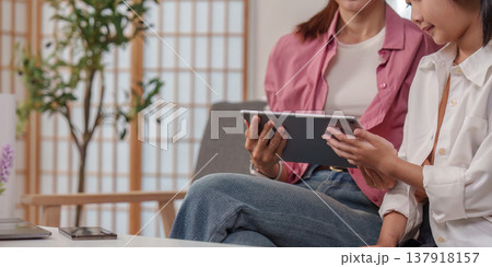 Mother and daughter using a tablet in a cozy living room Mother and daughter using a tablet in a cozy living room 137918157