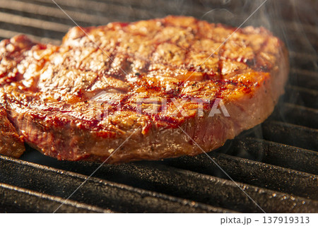 グリルで焼く前の生ステーキ 煙が上がる熱いグリル上 鉄板焼きの臨場感あるシーン 137919313