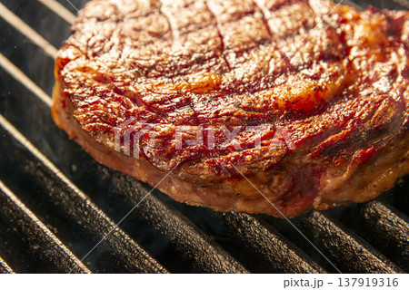 グリルで焼く前の生ステーキ 煙が上がる熱いグリル上 鉄板焼きの臨場感あるシーン グリルで焼く前の生ステーキ 煙が上がる熱いグリル上 鉄板焼きの臨場感あるシーン 137919316