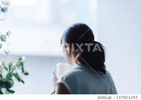 窓辺で飲み物を飲む女性の後ろ姿 窓辺で飲み物を飲む女性の後ろ姿 137921243