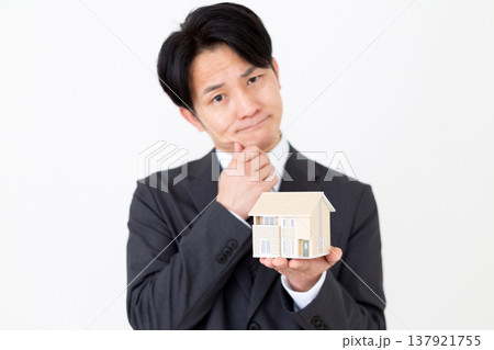 一戸建ての住宅模型を持って悩むミドル男性ビジネスマン 一戸建ての住宅模型を持って悩むミドル男性ビジネスマン 137921755