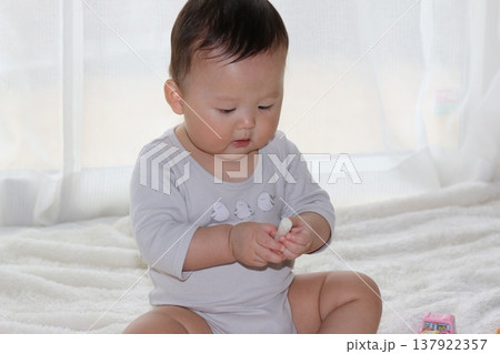 お座りしておやつを食べる9か月の赤ちゃん お座りしておやつを食べる9か月の赤ちゃん 137922357