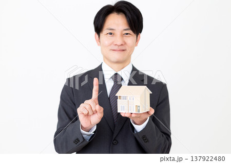 一戸建ての住宅模型を持って人差し指を立てるミドル男性ビジネスマン 137922480