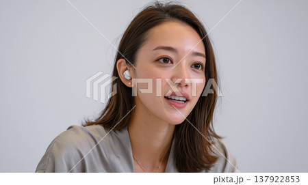 日中の明るい室内でワイヤレスイヤホンをつけてオンラインで会話しながら微笑んでいる女性 137922853