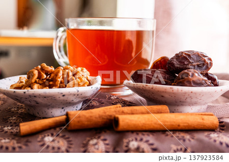 A close-up of two plates containing dates and walnuts, accompanied by cinnamon sticks prepared for Iftar at Ramadan. The scene highlights healthy snacks and natural ingredients. 137923584