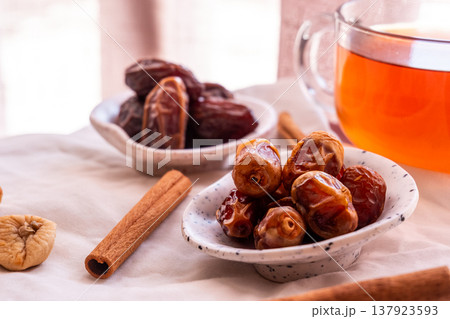 A close-up of two plates containing dates and walnuts, accompanied by cinnamon sticks prepared for Iftar at Ramadan. The scene highlights healthy snacks and natural ingredients. 137923593