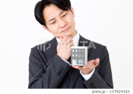 企業ビルの住宅模型を持って悩むミドル男性ビジネスマン 企業ビルの住宅模型を持って悩むミドル男性ビジネスマン 137924383