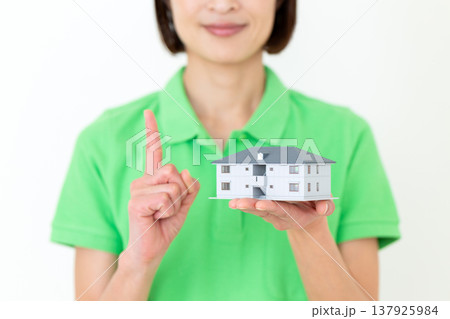 住宅模型を持って人差し指を立てるミドル女性の介護福祉士 137925984