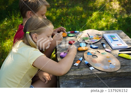 Using vibrant acrylics, children transform smooth, flat stones into colorful canvases for their imagination, creating perfect handmade gifts. Using vibrant acrylics, children transform smooth, flat stones into colorful canvases for their imagination, creating perfect handmade gifts. 137926152