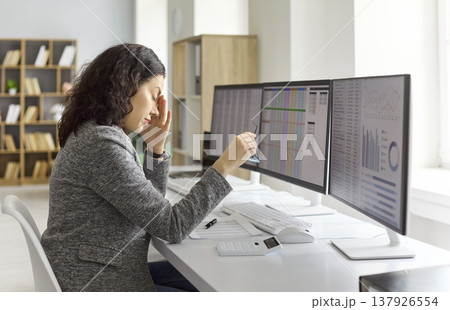 Tired female accountant massaging forehead at office computer during data analysis 137926554