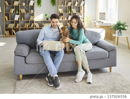 Happy couple with dog using laptop at home on sofa, remote work and leisure Happy couple with dog using laptop at home on sofa, remote work and leisure 137926556