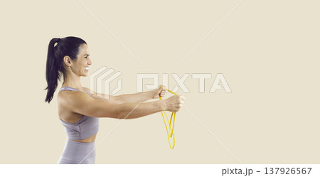 Fit woman training with yellow resistance band, side view on beige copy space Fit woman training with yellow resistance band, side view on beige copy space 137926567