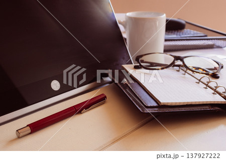 Workspace with laptop, planner, glasses, and a red pen for daily tasks symbolizing freelancing, and digital nomad lifestyle Workspace with laptop, planner, glasses, and a red pen for daily tasks symbolizing freelancing, and digital nomad lifestyle 137927222