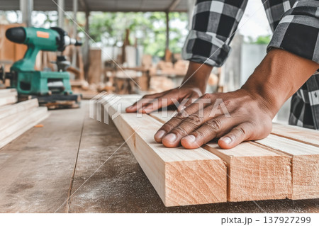 Skilled carpenter's hands align wooden planks on a workbench in a workshop, with power tools and wood shavings creating a realistic work environment 137927299