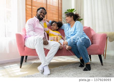 Joyful and playful multiethnic family of three sits together on pink sofa in living room at home Joyful and playful multiethnic family of three sits together on pink sofa in living room at home 137928093