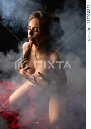 Sensual woman with an elegant hairstyle kneeling in smoke on red velvet fabric. 137928271
