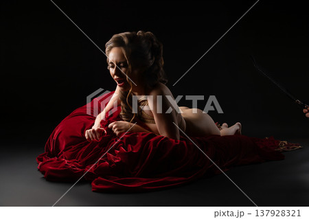Passionate woman in artistic rope bondage lying on rich red velvet in a dark studio setting. Passionate woman in artistic rope bondage lying on rich red velvet in a dark studio setting. 137928321