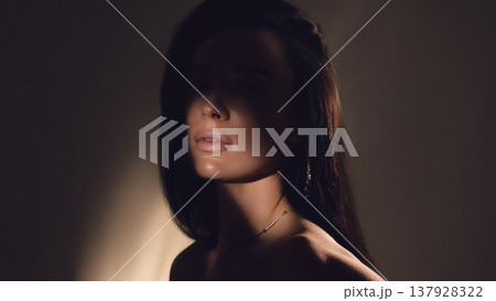 Low key portrait of woman with shadow across face in studio lighting. 137928322
