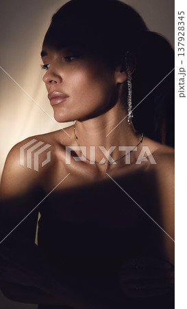 Woman with long earrings and glowing skin in dramatic studio lighting portrait. Woman with long earrings and glowing skin in dramatic studio lighting portrait. 137928345