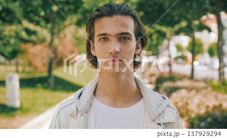 Closeup portrait of handsome confident young man at the park in summer. Confident teenager looks to the camera, outdoor portrait. Handsome face of a male model with brown hair at city. One person Closeup portrait of handsome confident young man at the park in summer. Confident teenager looks to the camera, outdoor portrait. Handsome face of a male model with brown hair at city. One person 137929294