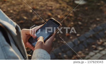 Person in the park is typing a text message. Human in the park typing a text message on a mobile phone. Male person looks into a cell phone and types a text sms. People and technology. Person in the park is typing a text message. Human in the park typing a text message on a mobile phone. Male person looks into a cell phone and types a text sms. People and technology. 137929343