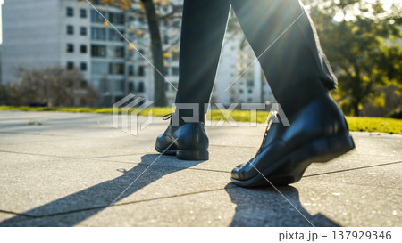 Legs of a businessman in fashionable shoes walking outdoors. Business concept. Close-up view to the businessman in a black new shoes walks on the street. Stylish men wears. Low angle. Rear view. Legs of a businessman in fashionable shoes walking outdoors. Business concept. Close-up view to the businessman in a black new shoes walks on the street. Stylish men wears. Low angle. Rear view. 137929346