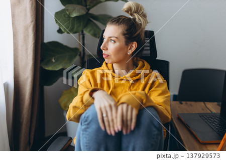 Sad woman sitting at home office looking away feeling burnout and loneliness in remote work lifestyle with soft daylight Sad woman sitting at home office looking away feeling burnout and loneliness in remote work lifestyle with soft daylight 137929573