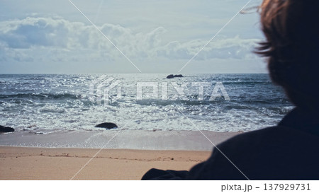 Young man stands on the empty sandy beach on the summer day and contemplating ocean water surface. Human stands on beach on a sunny day and looking to distance. Back view of Man on the ocean shore Young man stands on the empty sandy beach on the summer day and contemplating ocean water surface. Human stands on beach on a sunny day and looking to distance. Back view of Man on the ocean shore 137929731